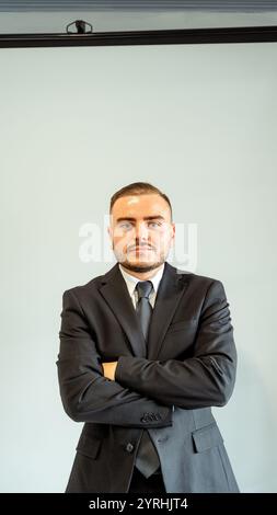 Un professionista latino sicuro in un'oscura tuta da lavoro con le braccia incrociate, che trasuda autorità e competenza, perfetto per aziende, legali o aziendali Foto Stock