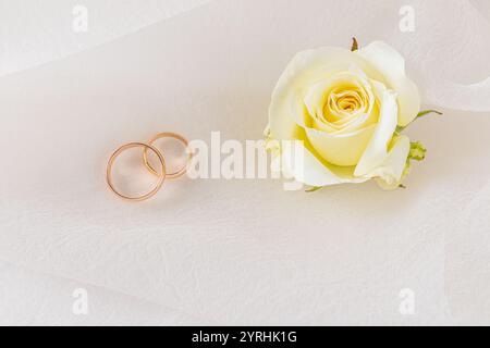 Un paio di fedi nuziali dorate poggiano su un lussuoso sfondo in raso, accompagnate da delicati fiori, a simboleggiare l'amore e l'impegno in un elegante, tim Foto Stock