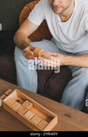 Un cieco interagisce con un puzzle di legno, concentrandosi sul miglioramento cognitivo e sulla consapevolezza. Il puzzle, con vari blocchi di forma, si trova su un bosco Foto Stock