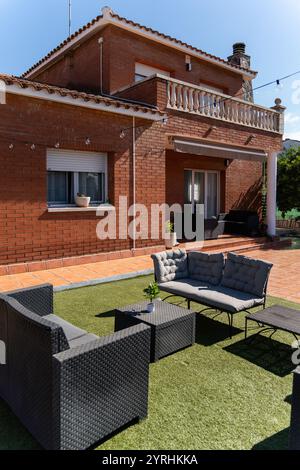 Moderna casa in mattoni con un accogliente patio con comodi posti a sedere all'aperto, la scena cattura uno spazio rilassato ideale per il tempo libero sotto un cielo azzurro Foto Stock