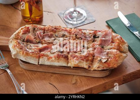 Gustosa pizza con focaccia condita con fette di prosciutto, funghi e formaggio fuso servita su una tavola di legno, rendendola uno spuntino perfetto o un pasto leggero Foto Stock