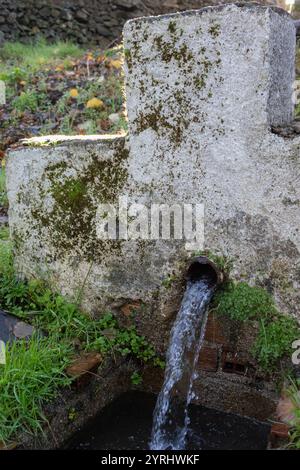 fonte naturale di acqua in natura con un grande flusso che esce da una piccola costruzione a podio indossata dal passare del tempo e circondata dalla natura Foto Stock