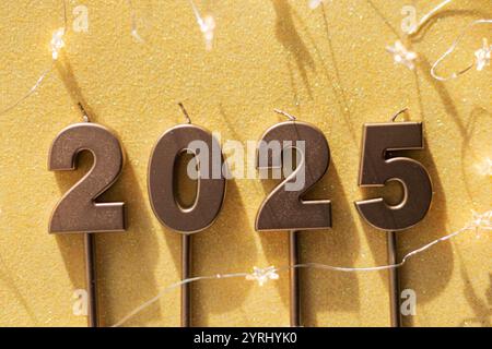 Le candele dorate festive 2025 con stelle luminose giacciono su uno sfondo dorato, vista dall'alto. Carta da parati per le feste. Capodanno 2025 e Natale Foto Stock