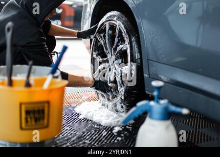 L'uomo professionista lava auto e ruote, cerchioni e pneumatici presso lo studio di dettaglio Foto Stock