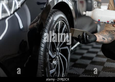 Un uomo con una spugna annerisce le gomme di un'auto in un garage. Sala di lavaggio auto e dettagli Foto Stock