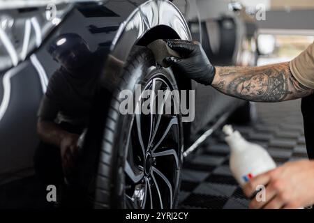 Uomo professionista che lava auto e ruote in garage. Dettagli. Cura degli pneumatici Foto Stock