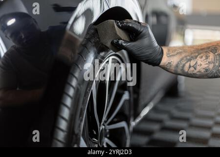 Uomo professionista che lucida pneumatici con spugna in garage. Studio dettagliato e lavaggio delle ruote Foto Stock