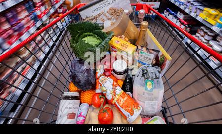 Colonia, Germania. 4 dicembre 2024. Un carrello completo con anatra polacca, verdure, frutta, stollen natalizi, gnocchi, vino frizzante, vino, cioccolatini e cioccolato Santas vengono sparsi oltre gli scaffali di un supermercato (sfocati a causa della lunga velocità dell'otturatore). (Al sondaggio dpa: "Every Second Person Saving on food shopping for Christmas") credito: Rolf Vennenbernd/dpa/Alamy Live News Foto Stock