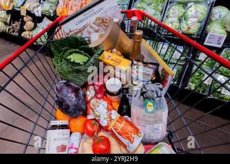 Colonia, Germania. 4 dicembre 2024. Un carrello completo con anatra polacca, verdure, frutta, stollen natalizi, gnocchi, vino frizzante, vino, cioccolatini e cioccolato Santas sono stati superati gli scaffali di un supermercato. (Al sondaggio dpa: "Every Second Person Saving on food shopping for Christmas") credito: Rolf Vennenbernd/dpa/Alamy Live News Foto Stock