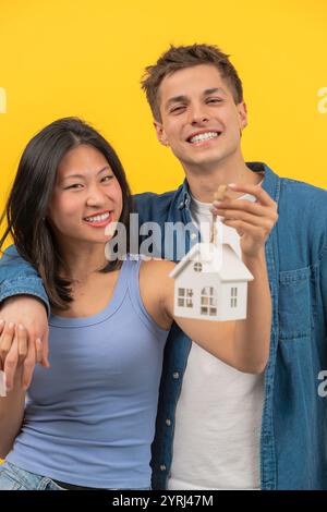 Coppia felice che tiene in mano le chiavi di casa e una piccola casa modello, per celebrare la nuova casa Foto Stock