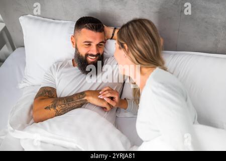 La mattina, una giovane coppia felice e amorevole è sdraiata a letto. Sono rilassanti e sorridenti. Foto Stock