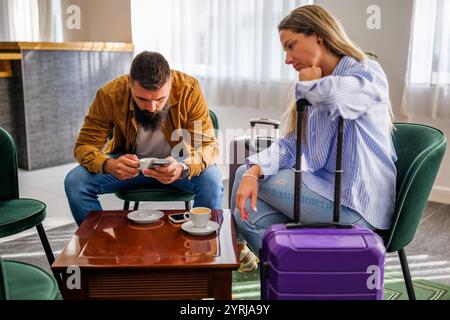 La giovane coppia va in vacanza. Turisti seduti al bar dell'aeroporto a causa del ritardo del volo. Foto Stock