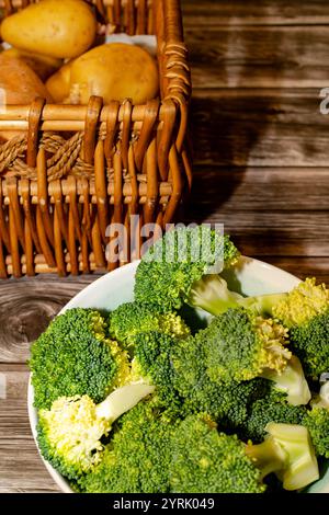 Broccoli a pezzi nel recipiente e patate nel cestello posto sul tavolo Foto Stock