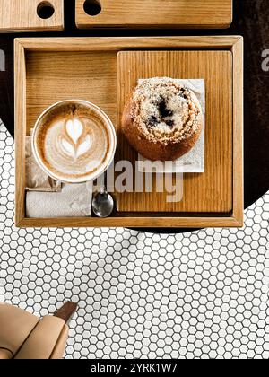 Un vassoio di legno con una tazza di cappuccino con latte art, un cucchiaio e una pasticceria appena sfornata posta su un tovagliolo. Vista dall'alto. Copia spazio Foto Stock