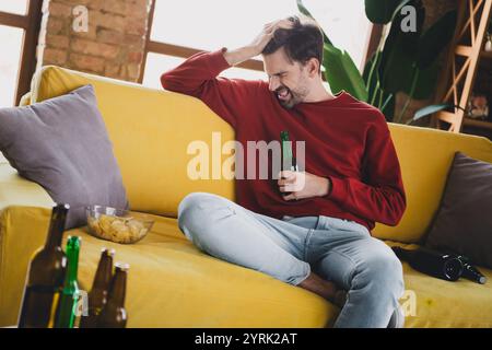 Giovane che si gode un weekend rilassante a casa con birra e spuntini in un accogliente appartamento. Foto Stock