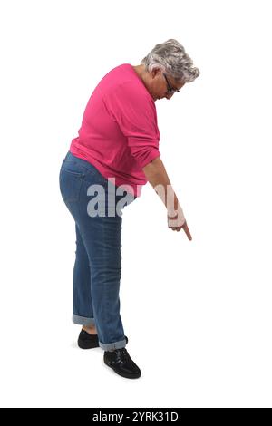 vista laterale di una donna anziana accovacciata che guarda verso il basso e punta il dito a terra su sfondo bianco Foto Stock