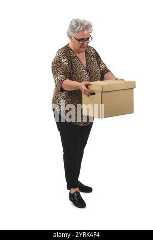 vista laterale della donna anziana che tiene in mano una scatola di cartone e la guarda su sfondo bianco Foto Stock