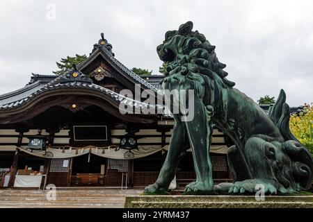 Una splendida statua di bronzo del leone guardiano splendidamente realizzata si erge graziosamente vicino a uno storico tempio giapponese Foto Stock