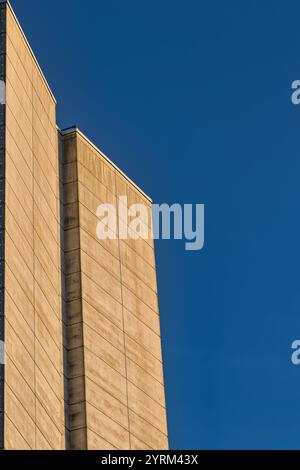 Una vista ravvicinata della facciata abbronzata di un edificio, con pannelli angolati contro un cielo limpido e blu profondo. L'immagine enfatizza le linee geometriche e l'architettura pulita Foto Stock