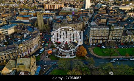 Vista aerea del centro della città con una ruota panoramica situata in una piazza circondata da edifici, strade e auto parcheggiate. Gli alberi autunnali sono visibili Foto Stock