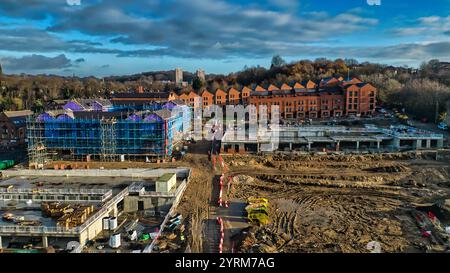 Vista aerea di un cantiere con un edificio parzialmente completato avvolto da impalcature blu, nuove case in mattoni e ampie opere di terra Foto Stock