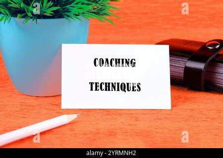 Concetto di business e sviluppo. TECNICHE DI COACHING con testo concettuale scritte su un biglietto da visita bianco su sfondo arancione. Foto Stock