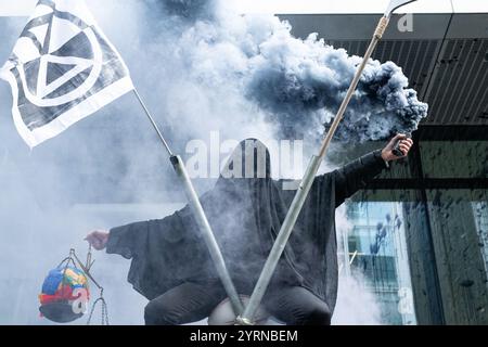 Londra, Regno Unito. 4 dicembre 2024. Un uomo seduto in cima a un treppiede vestito da mietitore fa scoppiare un fuoco di fumo mentre gli attivisti per il clima dall'estinzione la ribellione protesta contro l'ufficio londinese dello studio legale globale A&o Shearman, le cui finestre erano rovinate dal petrolio finto, chiedendo alla società di "tagliare i legami" con le società di combustibili fossili che rappresenta. Crediti: Ron Fassbender/Alamy Live News Foto Stock