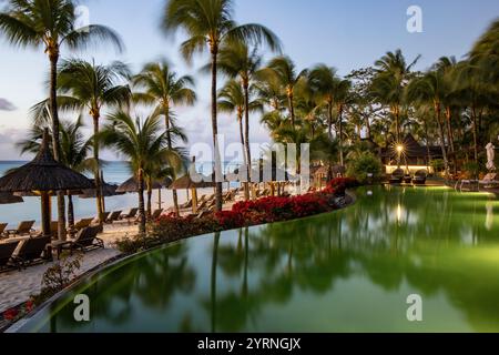 Piscina e ombrelloni di palapa dal tetto di paglia con palme da cocco al Royal Palms Beachcomber Luxury al tramonto, Grand Baie, Rivière du Rempart, Mauritius, i Foto Stock