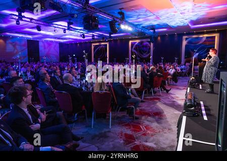 Jo Brand parla con un microfono a una grande sala di persone che cenano Foto Stock