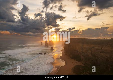 Una vista magica dei 12 Apostoli in Australia. Il sole splende attraverso nuvole lontane sull'oceano, con onde che si infrangono contro le formazioni. Un pa Foto Stock
