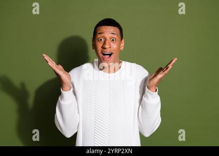 Giovane uomo in maglione bianco che esprime sorpresa su sfondo cachi Foto Stock