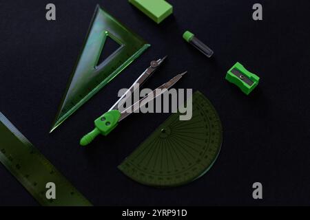 set di strumenti di geometria verde: righelli, bussole, gomma e nitidezza giacciono su uno sfondo nero. Matematica e lezione a scuola Foto Stock