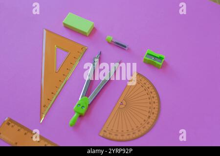 set di strumenti di geometria verde: righelli, bussole, gomma e nitidezza si trovano su uno sfondo rosa Foto Stock