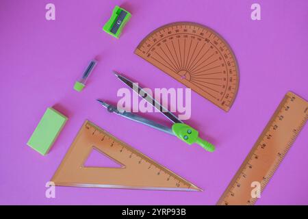 set di strumenti di geometria verde: righelli, bussole, gomma e nitidezza si trovano su uno sfondo rosa Foto Stock