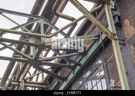 Struttura metallica che supporta le tubazioni su una vecchia parete in mattoni in un ambiente industriale Foto Stock