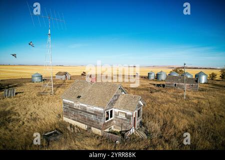 Una casa è in mezzo a un campo con qualche altra casa e un fienile. La casa è vecchia e abbandonata Foto Stock