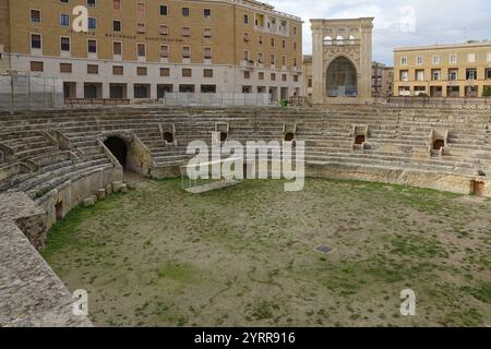 Un antico anfiteatro romano in pietra con all'interno erba, circondato da edifici storici, Lecce, Puglia, Italia, Europa Foto Stock