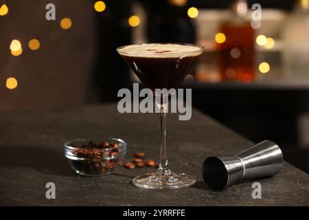 Bicchiere con deliziosi martini espresso, chicchi di caffè e jigger sul tavolo del bar Foto Stock