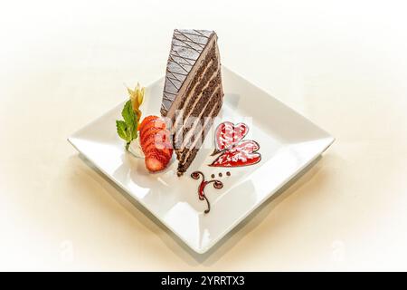 Una fetta di torta con fragole e salsa al cioccolato su un piatto bianco. La torta è tagliata in sei pezzi ed è ricoperta da un design a forma di cuore Foto Stock