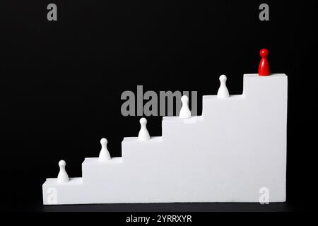Vincitore. Pezzo rosso tra quelli bianchi sulle scale su sfondo nero Foto Stock