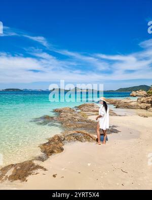Le limpide acque turchesi si infrangono dolcemente contro le sabbie dorate dell'Isola di Samae San. Un viaggiatore in una copertura bianca gode di splendide vedute costiere, circondato da rocce e colline lontane. Foto Stock