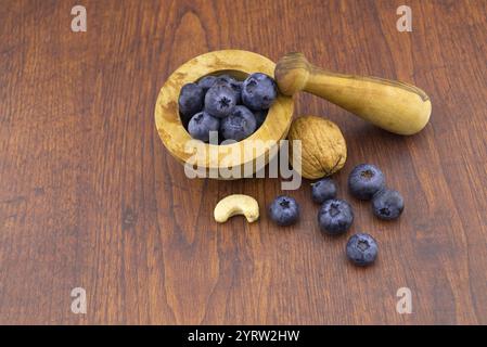 Pestello e mortaio in legno con noci, anacardi e mirtilli freschi su un tavolo di legno con imitspazio in un concetto di dieta e nutrizione sana, hi Foto Stock