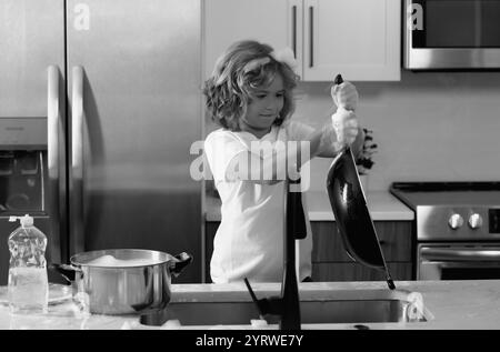 Divertenti ragazzi gemelli che aiutano in cucina con piatti di lavaggio. Bambini che si divertono con i lavori di casa. Bambino che lava i piatti nel lavello della cucina. Foto Stock