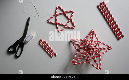 Stelle fatte di cannucce per cocktail. Con strisce rosse e bianche. Ago e filo bianco, forbici, provette per cocktail di diverse lunghezze. Sul backgrou bianco Foto Stock