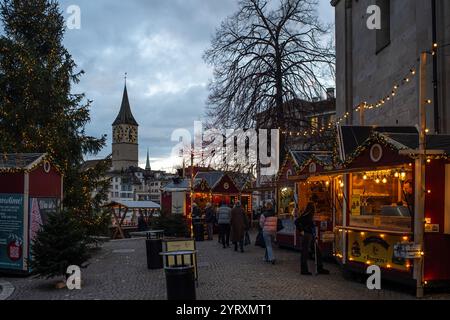 3-12-2024 Zurigo, Svizzera. Persone che visitano i negozi pop-up al mercato di Natale vicino alla chiesa di Grossmunster in serata. Foto Stock