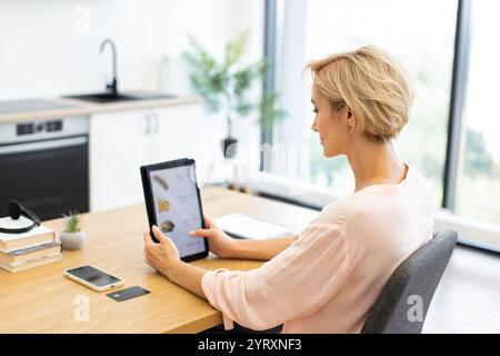 Donna caucasica che usa un tablet per ordinare cibo online in un ambiente domestico moderno. La scena casual mostra la tecnologia digitale che migliora la vita quotidiana. Foto Stock