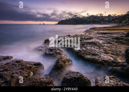 Le onde si infrangono dolcemente sulle coste rocciose di Crescent Bay Beach durante il tramonto, creando un'atmosfera serena su Laguna Beach, California. Foto Stock