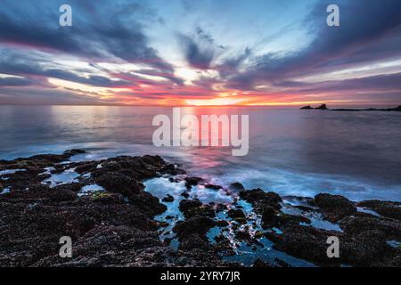 Ammira il tramonto mozzafiato a Crescent Bay Beach, dove acque tranquille si incontrano con i cieli vibranti a Laguna Beach, California. Foto Stock