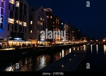 Vista notturna sul lungomare di edifici moderni illuminati e riflessi sul fiume Motlawa. Danzica, Polonia - 19 maggio 2024 Foto Stock