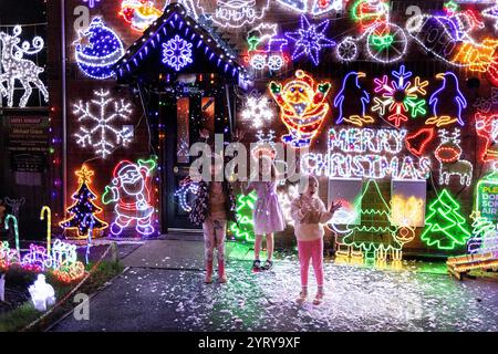 Minehead, Regno Unito. 4 dicembre 2024. Questa è la casa più festosa della Gran Bretagna? Bambini che giocano con la neve, da una macchina da neve, che è una delle caratteristiche della casa. Michael Grace, ha passato gli ultimi dieci anni aumentando dolcemente la quantità di luci natalizie nella sua proprietà a Plover Close a Minehead, Somerset, per far brillare il suo display! Le luci si stanno rivelando un grande richiamo per i visitatori, da quando sono stati accesi il 23 novembre, e stanno raccogliendo fondi vitali per l'ambulanza Dorset e Somerset Air. Credito: Mark Passmore/Alamy Live News Foto Stock